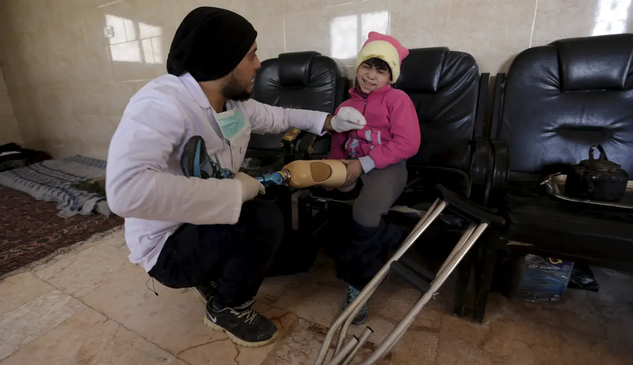 Seorang pekerja pembuat anggota badan buatan, Khamis (kiri) saat memasangkan kaki palsu kepada seorang bocah di kota Maaret al - Numan di provinsi Idlib , Suriah 20 Maret 2016. (REUTERS / Khalil Ashawi)