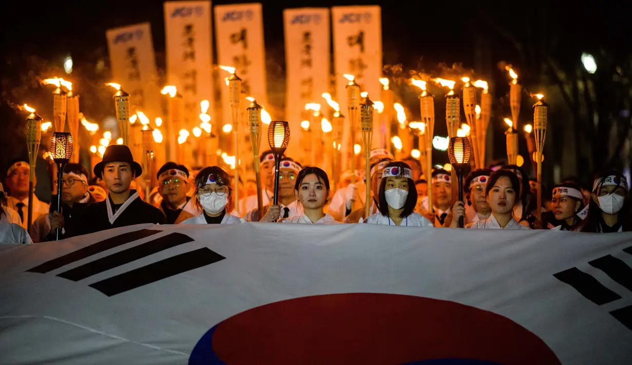 Peserta mengenakan kostum tradisional sambil memegang obor api, saat berbaris untuk merayakan peringatan Gerakan Kemerdekaan 1 Maret di Cheonan, 90 kilometer selatan Seoul pada 28 Februari 2023. Warga Korea Selatan merayakan hari libur peringatan untuk menandai pemberontakan sipil 1919 melawan Pemerintahan kolonial Jepang dari tahun 1910-1945. (AFP/Anthony Wallace)