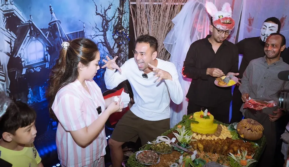 Dari kanal YouTube, Raffi dan Gigi terlihat digiring ke sebuah ruangan dengan mata tertutup. Setibanya di lokasi dan dan membuka mata, pasangan selebriti ini begitu terkejut melihat dekorasi ruangan yang sudah dihiasi lampu biru dan merah dengan nuansa horor. Mereka menyiapkan kue ulang tahun dan nasi kuning beserta lauk pauknya. (Liputan6.com/IG/@raffinagita1717)