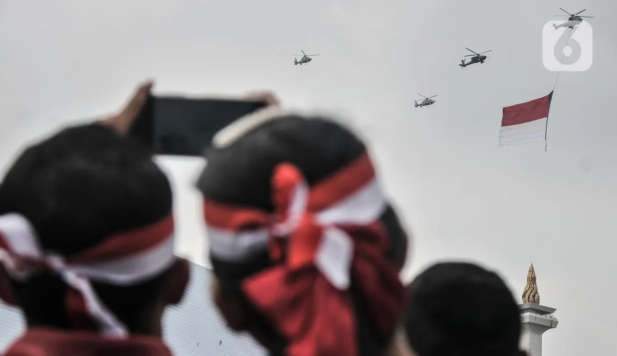 Warga menyaksikan manuver helikopter TNI AU membawa bendera Merah Putih saat perayaan HUT ke-77 Republik Indonesia (RI) di Taman Aspirasi Monumen Nasional (Monas), Jakarta Pusat, Rabu (17/8/2022).  Aksi akrobatik pesawat tempur dan helikopter yang membawa bendera Merah Putih tersebut disambut antusias oleh warga yang datang untuk mengikuti upacara Kemerdekaan RI. (merdeka.com/Iqbal S Nugroho)