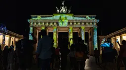 Orang-orang mengambil foto Gerbang Brandenburg yang diterangi cahaya dalam Festival of Lights di Berlin pada 14 September 2020. Kreasi cahaya lebih dari 90 karya seni tersebut ditampilkan di 86 lokasi yang berlangsung hingga 20 September mendatang. (John MACDOUGALL/AFP)