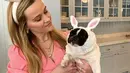 Reese Whiterspoon tampil manis di Paskah kali ini. Ia mengenakan dress lengan pendek kotak-kotak merah muda, mengenakan bando telinga kelinci yang juga bernuansa merah muda, menggendong anjing peliharaannya yang diberi kostum telinga kelinci yang menggemaskan. Foto: Instagram.