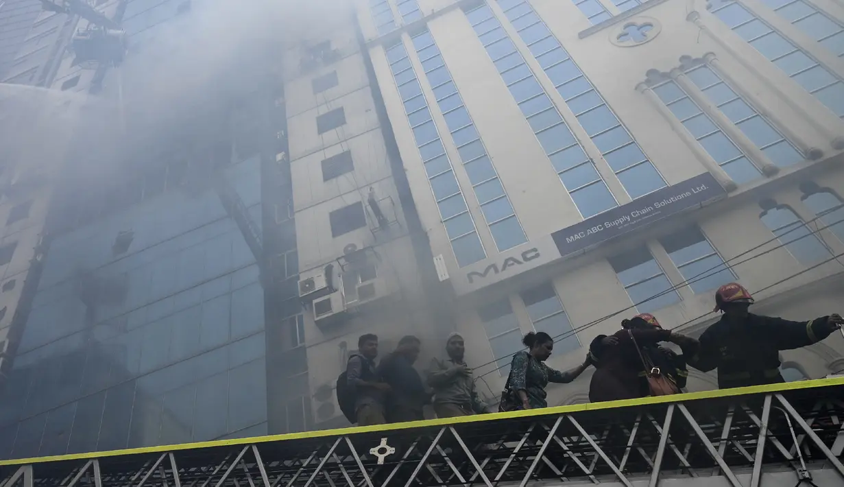 Petugas pemadam kebakaran Bangladesh menuntun orang menuruni tangga di bawah gedung kantor yang terbakar di Dhaka (28/3). Kebakaran besar melanda gedung perkantoran yang menewaskan sedikitnya lima orang dan lainnya masih terperangkap dalam gedung yang terbakar tersebut. (AFP/Munir Uzzaman)