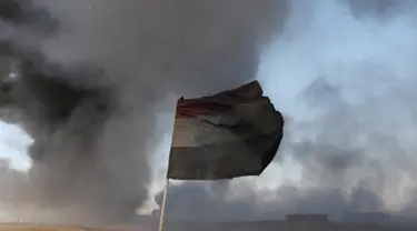 Sebuah bendera Irak terlihat di depan ladang minyak yang dibakar oleh ISIS di Qayyara, selatan Mosul, Irak, (23/11).Sebelumnya, sekitar enam sumur minyak telah dibakar ISIS di kawasan tersebut. (REUTERS/Goran Tomasevic)