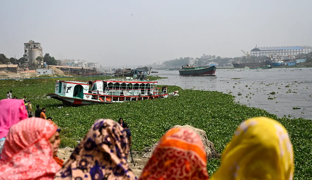 Orang-orang menonton feri yang diselamatkan setelah kecelakaan di Sungai Shitalakshya di Narayanganj, Bangladesh (21/3/2022). Setidaknya enam mayat ditemukan dan 20 orang masih hilang setelah sebuah feri terbalik di sungai Shitalakkhya. (AFP/Munir uz Zaman)