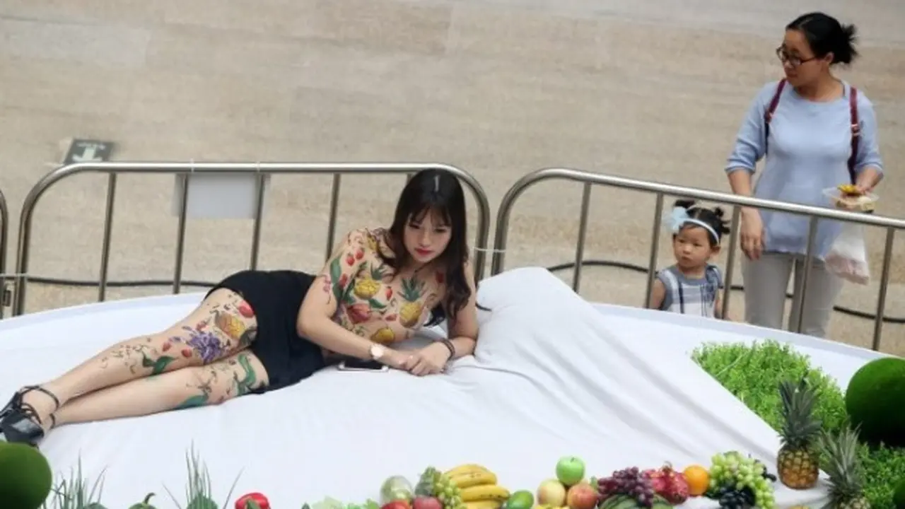 Seorang pengunjung tengah mengamati model yang nyaris bugil ditengah-tangah hamparan buuah. Foto : Shanghaiist