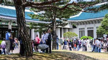 Sepasang suami istri (tengah) berswafoto saat pengunjung lain mengantre untuk berfoto di depan Blue House (belakang) sehari setelah kompleks tersebut dibuka untuk umum sesuai janji kampanye Presiden Korea Selatan Yoon Suk-yeol di Seoul, Korea Selatan, 11 Mei 2022. (ANTHONY WALLACE/AFP)