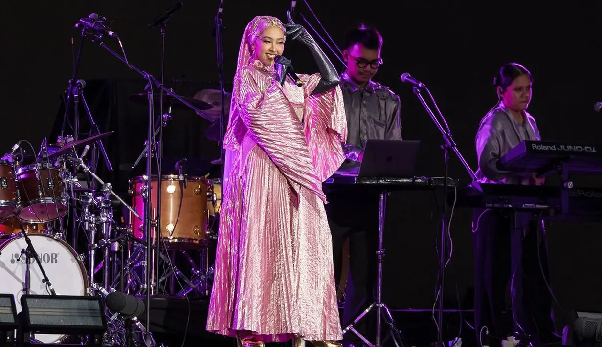 Di konser Coldplay, Jinan tampil menawan dengan gaun pleated pink satin dan latex gloves hitam. Dipadukan dengan hijab senada dengan headpiece yang artsy. [@livenationsg]