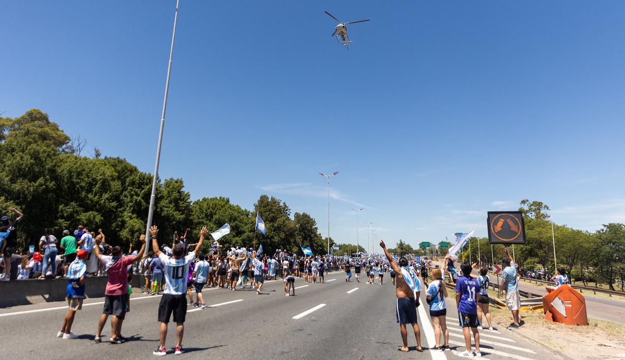 Masyarakat Argentina memberikan sambutan kepada beberapa anggota timnas Argentina yang berada di dalam helikopter saat parade kemenangan Piala Dunia 2022 di provinsi Buenos Aires, pada 20 Desember 2022. Messi dan kolega terpaksa dievakuasi karena bus yang mereka gunakan tak bisa mencapai lokasi yang direncanakan akibat membeludaknya warga di jalanan. (AFP/Tomas Cesta)