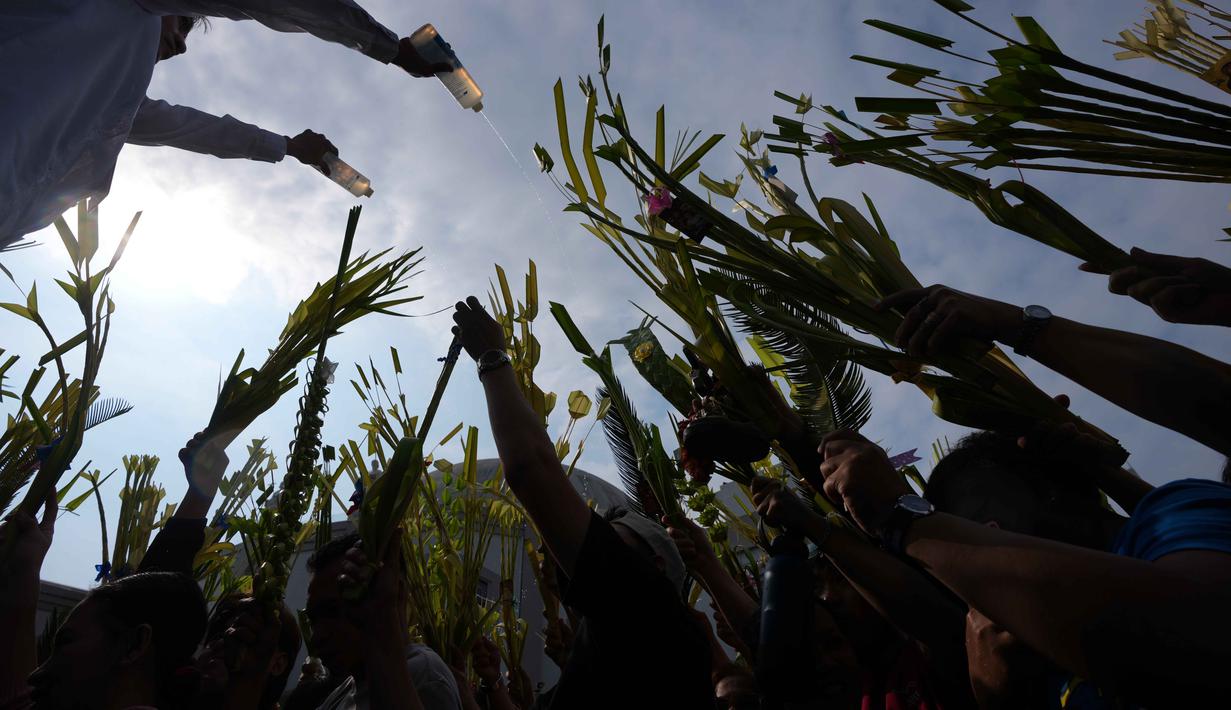 Hari ini, Minggu 29 Maret 2026, merupakan pekan terakhir sebelum perayaan Paskah. Tampak dalam foto, seorang pekerja gereja menggunakan botol untuk memercikkan air suci ke daun palem para umat selama upacara pemberkatan di luar Katedral Antipolo, kota Antipolo, provinsi Rizal, Filipina, saat memperingati Minggu Palma, 29 Maret 2026. (AP Photo/Aaron Favila)