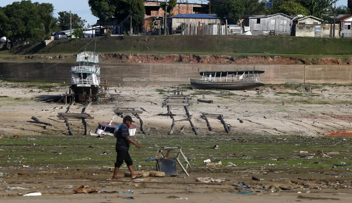 Seorang pria berjalan dan perahu di lahan kering di daerah yang terkena dampak kekeringan dekat Sungai Solimões, Tefe, Amazonas, Brasil, Rabu (19/10/2022). Pemerintah setempat mengatakan terdapat 17 kota dalam status waspada, 39 kota status siaga, dan 3 lainnya dalam keadaan darurat kekeringan. (AP Photo/Edmar Barros)