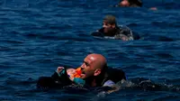 Seorang pengungsi Suriah menggendong bayi sambil berenang menuju pantai setelah perahu yang mereka naiki kempes sebelum mencapai pulau Yunani Lesbos, 12 September 2015. (REUTERS/Alkis Konstantinidis)  