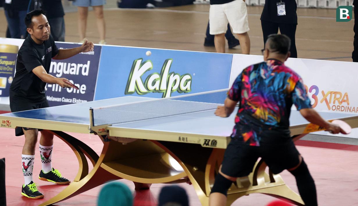 Denny Cagur (kiri) memakai kostum unik saat bertanding tenis meja melawan Cing Abdel di Turnamen Olahraga Selebriti Indonesia yang berlangsung di GOR Universitas Negeri Jakarta, Sabtu (29/7/2023).  Denny Cagur terlihat memakai kaos kaki berwarna putih dengan logo ayam jago yang biasa digunakan di mangkok. (Bola.com/Abdul Aziz)