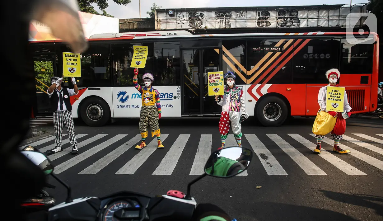 Angggota Komunitas Aku Badut Indonesia (ABI) melakukan aksi kampanye penggunaan di kawasan Cilandak, Jakarta Selatan, Senin (12/7/2021). Selain itu, mereka juga membagi-bagikan masker secara gratis bagi para pengendara motor yang melintas. (Liputan6.com/Johan Tallo)