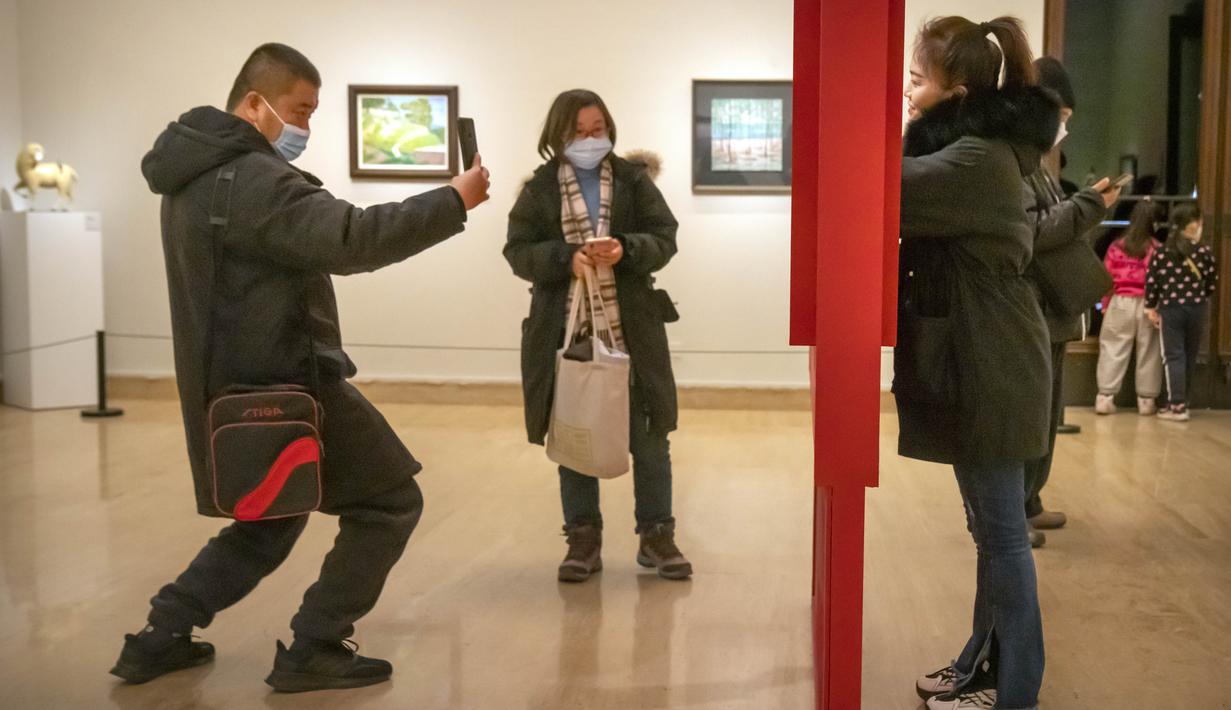 Seorang perempuan berpose untuk foto di galeri di Museum Seni Nasional China di Beijing, Rabu (1/2/2023). Pengunjung terus berduyun-duyun ke museum, situs bersejarah, dan tempat wisata di ibu kota China saat periode liburan Tahun Baru Imlek berakhir. (AP Photo/Mark Schiefelbein)