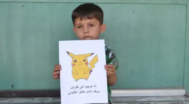 Seorang bocah Suriah memegang kertas bergambar karakter Pokemon bertuliskan "Aku di Kafr NABL di pedesaan Idlib, datang dan selamatkan aku", Suriah (22/7). (REUTERS)