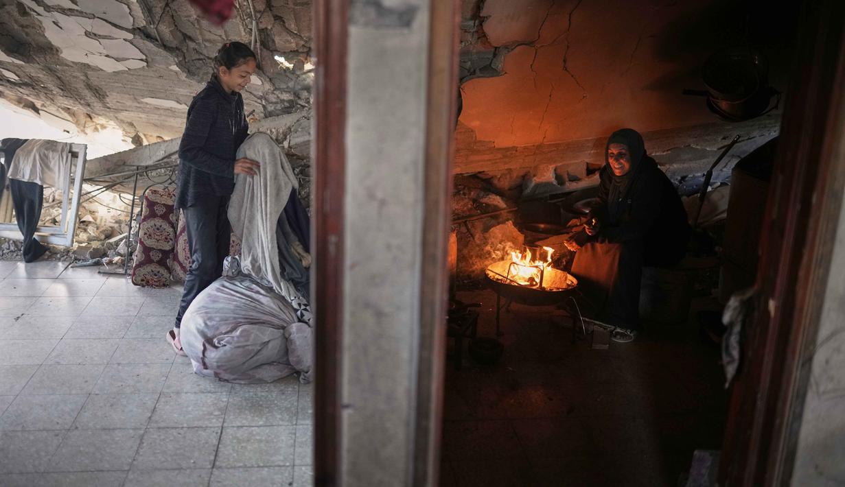 Warga Palestina di Kota Gaza mencoba bangkit dan membangun kembali, melanjutkan hidup meski hidup dalam kekurangan. Tampak dalam foto, Amani Halawa menyalakan api sementara putrinya, Aya, mengatur cucian di rumah mereka yang rusak di Jabaliya, Kota Gaza, Selasa, 25 November 2025. (AP Photo/Jehad Alshrafi)