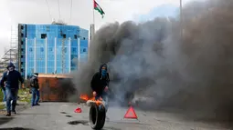 Demonstran Palestina membakar ban saat terjadi bentrokan menyusul demonstrasi di kota Ramallah Palestina (16/3). Mereka melakukan aksi menolak Yerusalem sebagai ibu kota Israel. (AFP Photo/Abbas Momani)