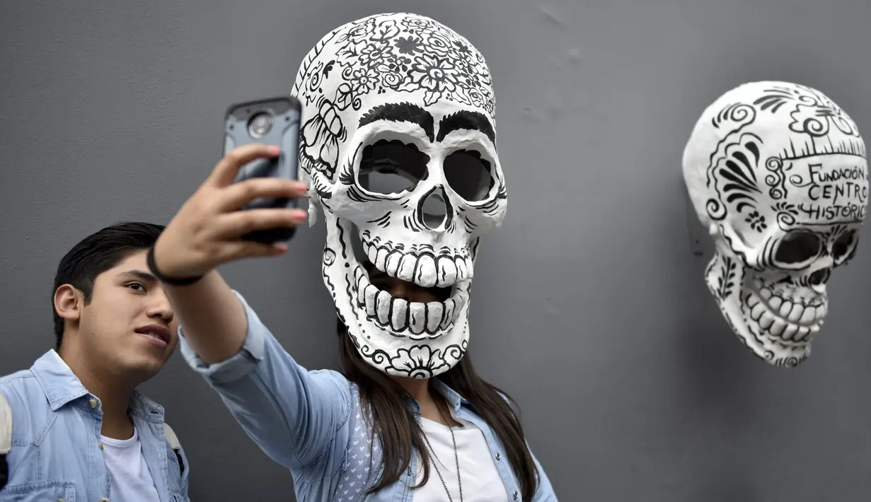 Seorang wanita berswafoto dengan replika tengkorak saat pameran dan kontes di perayaan Hari Kematian di Mexico City (1/11). Pameran dan kontes ini diadakan oleh Historic Center Foundation dalam rangka perayaan Hari Orang Mati. (AFP Photo/Yuri Cortez)