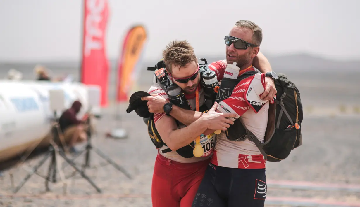 Seorang peserta membantu rekan satu timnya saat akan melewati garis finish dalam kompetisi Marathon des Sables ke-33 di gurun Sahara, Maroko (13/4). (AP Photo / Mosa'ab Elshamy)