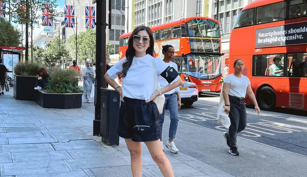 Nisya Ahmad berpose di samping bus di daerah London. Tampil bergaya santai mengenakan kaus putih zip-pocket Prada dan short pouch pants hitam serta kacamata fancy sebagai pemanisnya. Penampilan Nisya sangat kece maksimal. (Instagram/nissyaa)
