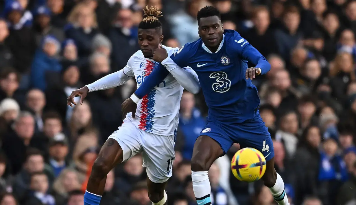 Pemain Chelsea, Benoit Badiashile (kanan) berebut bola dengan pemain Crystal Palace, Wilfried Zaha pada laga lanjutan Liga Inggris 2022/2023 di Stamford Bridge, London, 15 January 2023. Pemain berkebangsaan Prancis itu diboyong dari AS Monaco dengan harga 38 juta euro pada bursa transfer Januari 2023. (AFP/Ben Stansall)