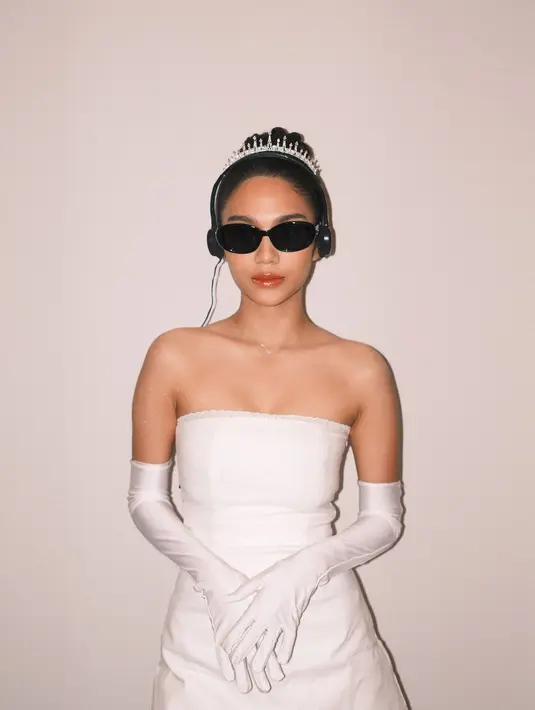 Azizah Salsha cosplay jadin Anne Hathaway di film Princess Diaries yang terkenal. Ia kenakan strapless dress dan gloves putih dipadukan dengan crown minimalis dan headphone [@azizahsalsha_]