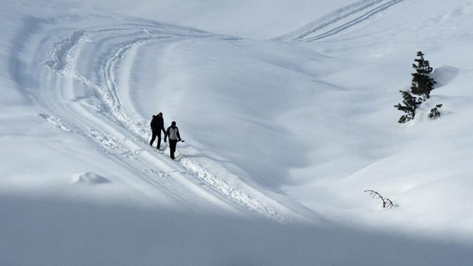 Orang-orang berjalan melewati salju di resor ski di Gulmarg, sekitar 55 km utara Srinagar, Jammu dan Kashmir, India, 25 Januari 2021. Ketika musim dingin tiba, perjalanan dari Srinagar ke Gulmarg akan menyuguhkan lansekap gunung-gunung berselimut salju yang kokoh dan beku. (Tauseef MUSTAFA/AFP)