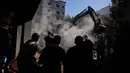 Orang-orang berkumpul saat sebuah ekskavator membersihkan puing-puing di lokasi serangan Israel pada Minggu 5 April 2026 terhadap sebuah bangunan di lingkungan Jnah, Beirut, Lebanon, Senin 6 April 2026. (AP Photo/Hassan Ammar)