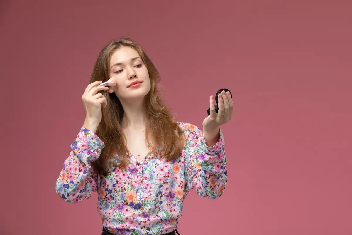 Seorang perempuan sedang mengaplikasikan makeup di bagian pipinya (Foto Dok: Freepik/KamranAydinov)