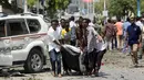 Sejumlah warga sipil membawa mayat seorang pria yang tewas di lokasi ledakan dekat sebuah hotel di Mogadishu, Somalia (28/3). (Reuters/Feisal Omar)