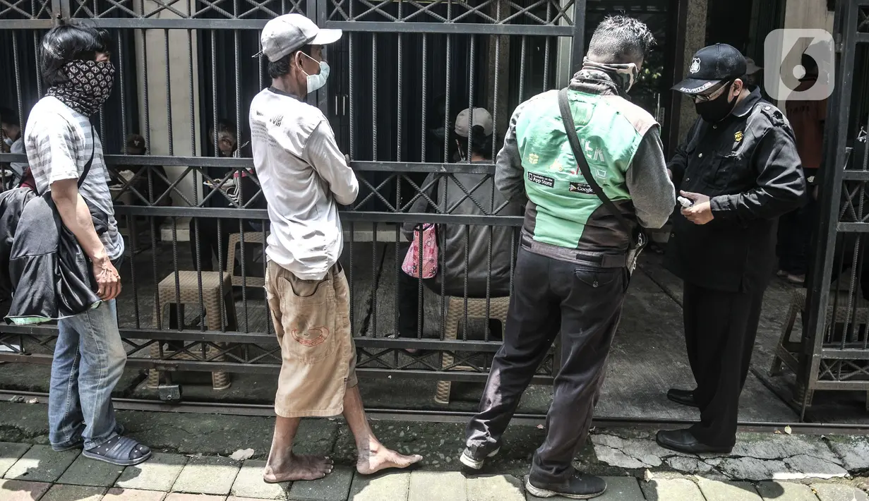 Petugas memeriksa suhu tubuh warga sebelum memasuki area layanan makan gratis di Jalan Basuki Rachmat, Cipinang Muara, Jakarta, Senin (8/3/2021). Sebagian besar yang datang mayoritas berprofesi kuli bangunan, pengamen, petugas taman kota hingga pengemudi ojek online. (merdeka.com/Iqbal S Nugroho)