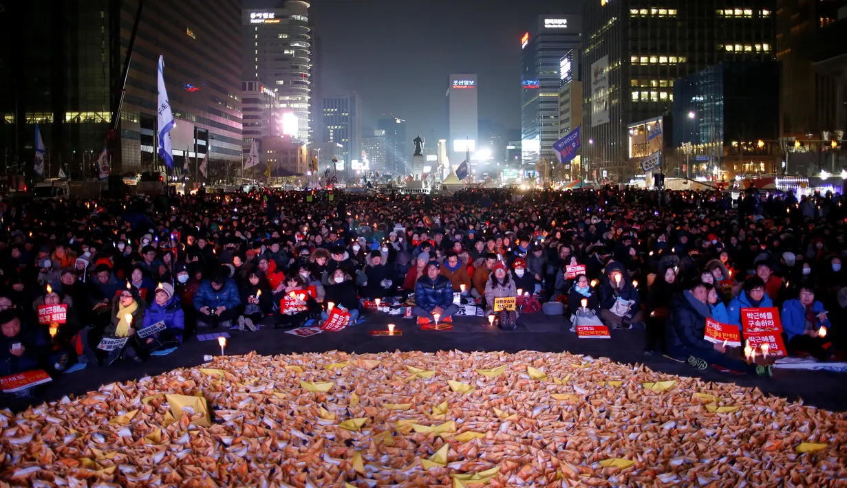 Sejumlah orang duduk di kapal kertas kuning yang didedikasikan untuk tragedi kapal feri Sewol selama unjuk rasa menuntut penggulingan Presiden Park Geun-hye pada malam pergantian tahun di Seoul, Korea Selatan (Korsel), Sabtu (31/12). (REUTERS/Kim Hong-Ji)