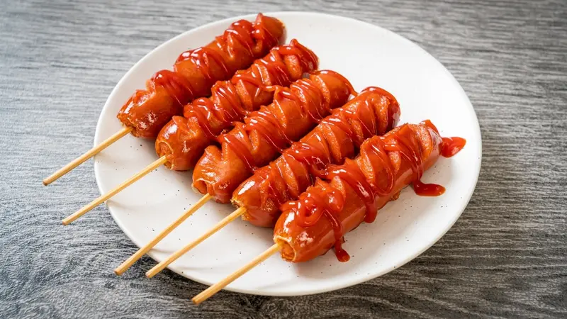 Sosis panggang keemasan yang gurih dengan aroma khas BBQ, disajikan hangat dengan saus sambal dan mayones