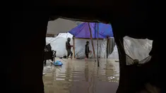 Para pengungsi Palestina berjalan melewati kamp tenda yang basah kuyup akibat hujan lebat di Deir al-Balah, Jalur Gaza tengah, Kamis, 26 Maret 2026. Kondisi kamp pengungsian di Gaza sangat memprihatinkan akibat banjir yang terus berulang selama musim dingin. (AP Photo/Abdel Kareem Hana)