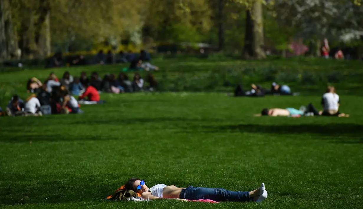 Seorang wanita tampak berjemur di sebuah taman di pusat kota London,  Inggris, Minggu (9/4). Sinar matahari hangat bersuhu 20 derajat celsius dimanfaatkan warga Inggris untuk berjemur di taman-taman kota. (AFP PHOTO / BEN STANSALL)