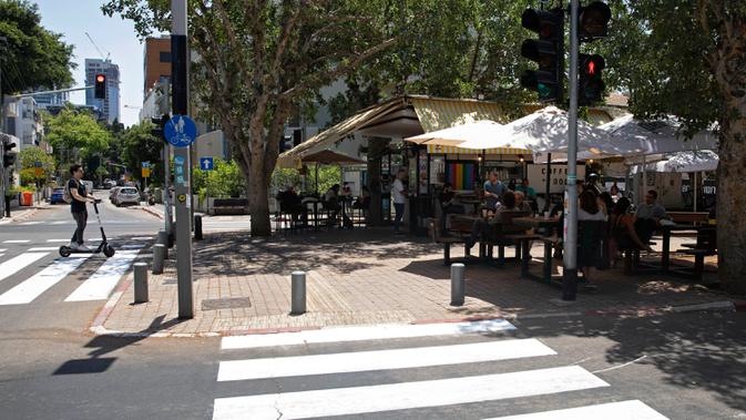 Warga Israel duduk di sebuah kedai kopi luar ruangan di Tel Aviv, Rabu (27/5/2020). Setelah lebih dari dua bulan ditutup untuk membendung penularan virus corona, restoran hingga kafe di Israel diizinkan dibuka kembali hari Rabu, 27 Mei. (AP Photo/Sebastian Scheiner)