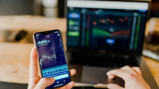 Seseorang Sedang Mengecek Grafik Investasi di Handphone dan Laptop