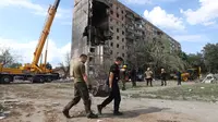 Tim penyelamat membawa pecahan rudal di luar bangunan perumahan sembilan lantai yang sebagian hancur akibat serangan rudal Rusia di Rig Kryvyi pada 31 Juli 2023, di tengah invasi Rusia ke Ukraina. (AFP/Ukrainian Emergency Service)
