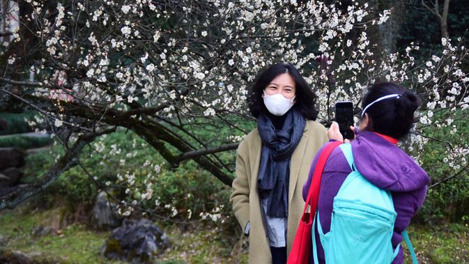 Seorang wanita berfoto di taman botani Hangzhou, Provinsi Zhejiang, China (19/2/2020). Sebagai upaya pencegahan coronavirus baru, kawasan indah tersebut telah menetapkan batas jumlah pengunjung saat ini dan semua yang memasuki kawasan itu diwajibkan mengenakan masker. (Xinhua/Zheng Mengyu)