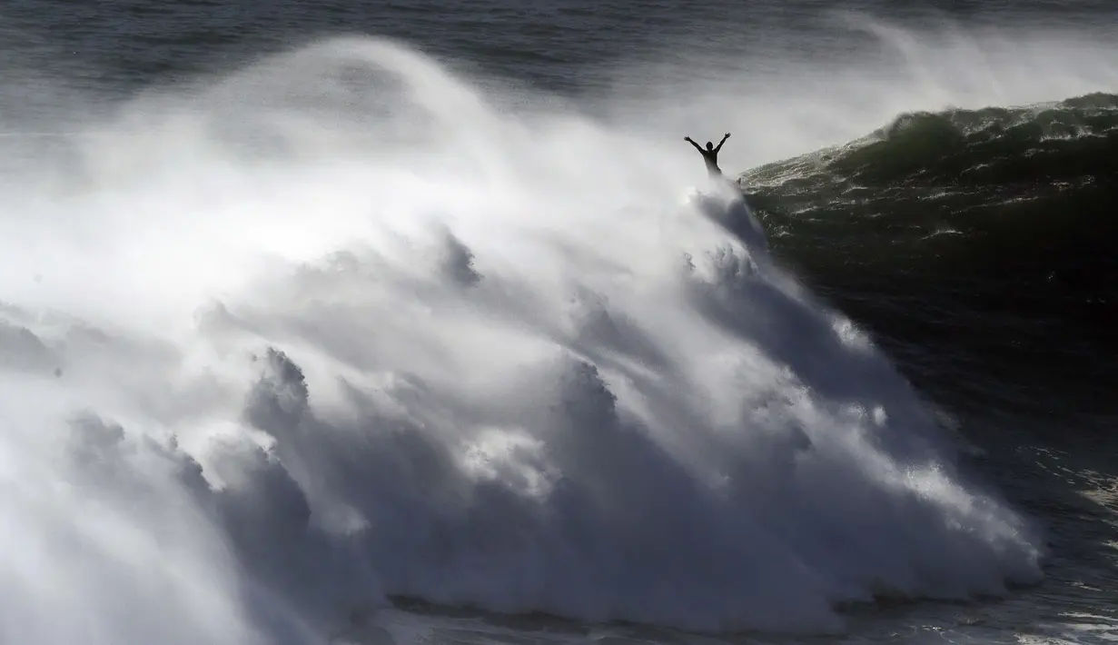 Seorang peselancar mengangkat tangannya saat keluar dari ombak selama sesi selancar derek di Praia do Norte atau Pantai Utara di Nazare, Portugal, Kamis (29/10/2020). (AP Photo/Pedro Rocha)