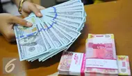 Petugas menunjukkan mata uang dolar dan mata uang rupiah di penukaran uang di Jakarta, Rabu (9/11). Nilai tukar rupiah terhadap dolar Amerika Serikat (AS) pada saat jeda siang ini kian terpuruk di zona merah. (Liputan6.com/Angga Yuniar)