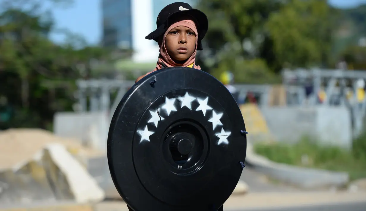 Seorang anak laki-laki membawa tameng berwarna hitam saat mengambil bagian dalam demonstrasi untuk menentang pemerintahan Presiden Nicolas Maduro, di Caracas (4/7). (AP Photo / Federico Parra)
