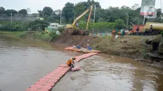 Pekerja Dinas Kebersihan mengangkat sampah kasur yang terjaring disaringan sampah dengan latar belakang alat berat sedang mengeruk lumpur Kali Pesanggrahan, Lebak Bulus, Jakarta Selatan, Rabu (4/11/2020). (merdeka.com/Dwi Narwoko)