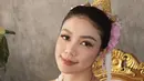 Pakaian adat Chut Thai yang dikenakan Regina terdiri dari tube top putih yang dipadukan dengan kain tenun coklat keemasan. Dihiasi dengan sabuk emas tradisional yang berkilau, penampilannya semakin memikat hati para penggemar. Aksesori emas yang melengkapi penampilannya, seperti mahkota kecil, anting, gelang, dan kalung dengan liontin besar, semakin memperkuat kesan kerajaan dan elegan.  (Liputan6.com/IG/@reginaaphx)