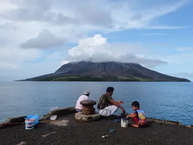 Orang-orang memancing di pelabuhan di pulau Tagulandang di Sitaro, Sulawesi Utara dengan latar belakang gunung berapi Ruang yang mengeluarkan asap, Jumat (19/4/2024). (Ronny Adolof BUOL / AFP)