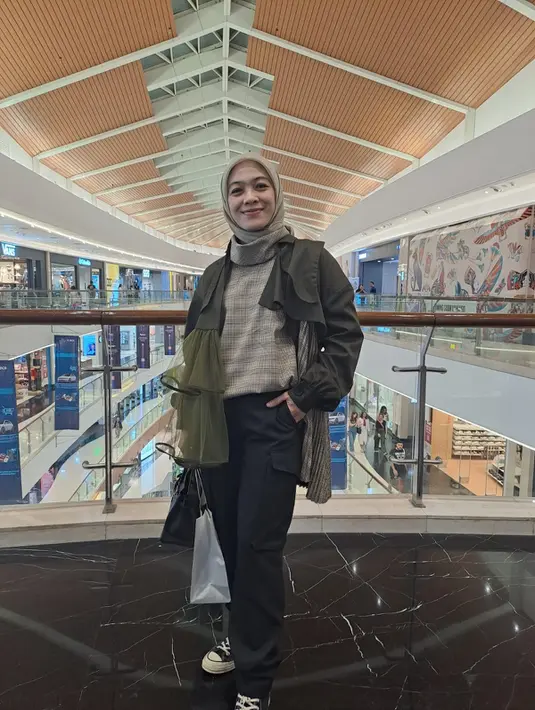 Dian Ayu Lestari mengenakan outer plisket hijau army dari IKYK dipadukan kerudung dan atasannya, serta celana hitam. Dengan sepatu Converse dan tas hitam Hermesnya.. [Anisha Saktian]