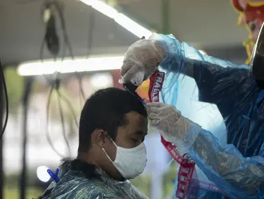 Tukang cukur mengenakan alat pelindung diri (APD) dari plastik saat mencukur rambut pelanggan di Pondok Kelapa, Jakarta, Selasa (5/5/2020). Tukang cukur mengenakan APD untuk mengurangi risiko penularan virus corona COVID-19. (merdeka.com/Imam Buhori)