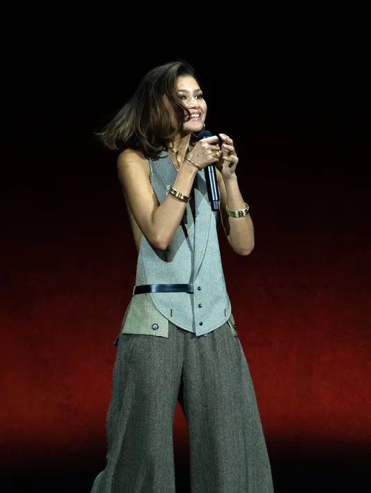 Zendaya melengkapi penampilannya dengan celana warna abu-abu gelap yang hangat, ditambah sepatu pump putih, tumpukan gelang metalik, dan anting-anting emas besar. (AFP/VALERIE MACON)