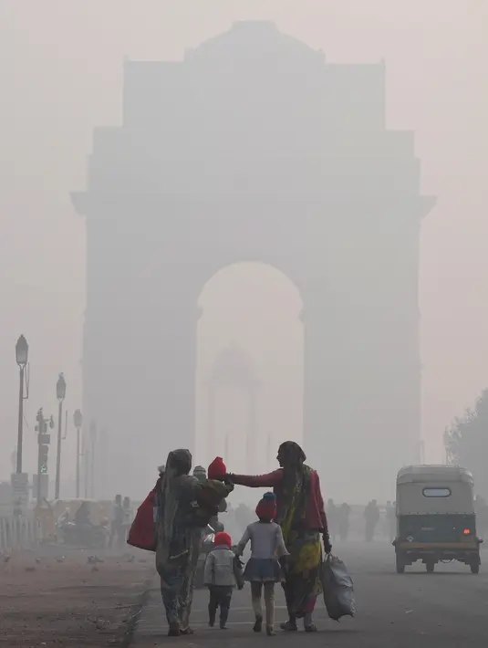 Perempuan India berjalan bersama anak-anak mereka di tengah kabut tebal di dekat Gerbang India di New Delhi  (24/12). (AFP Photo/Prakash Singh)